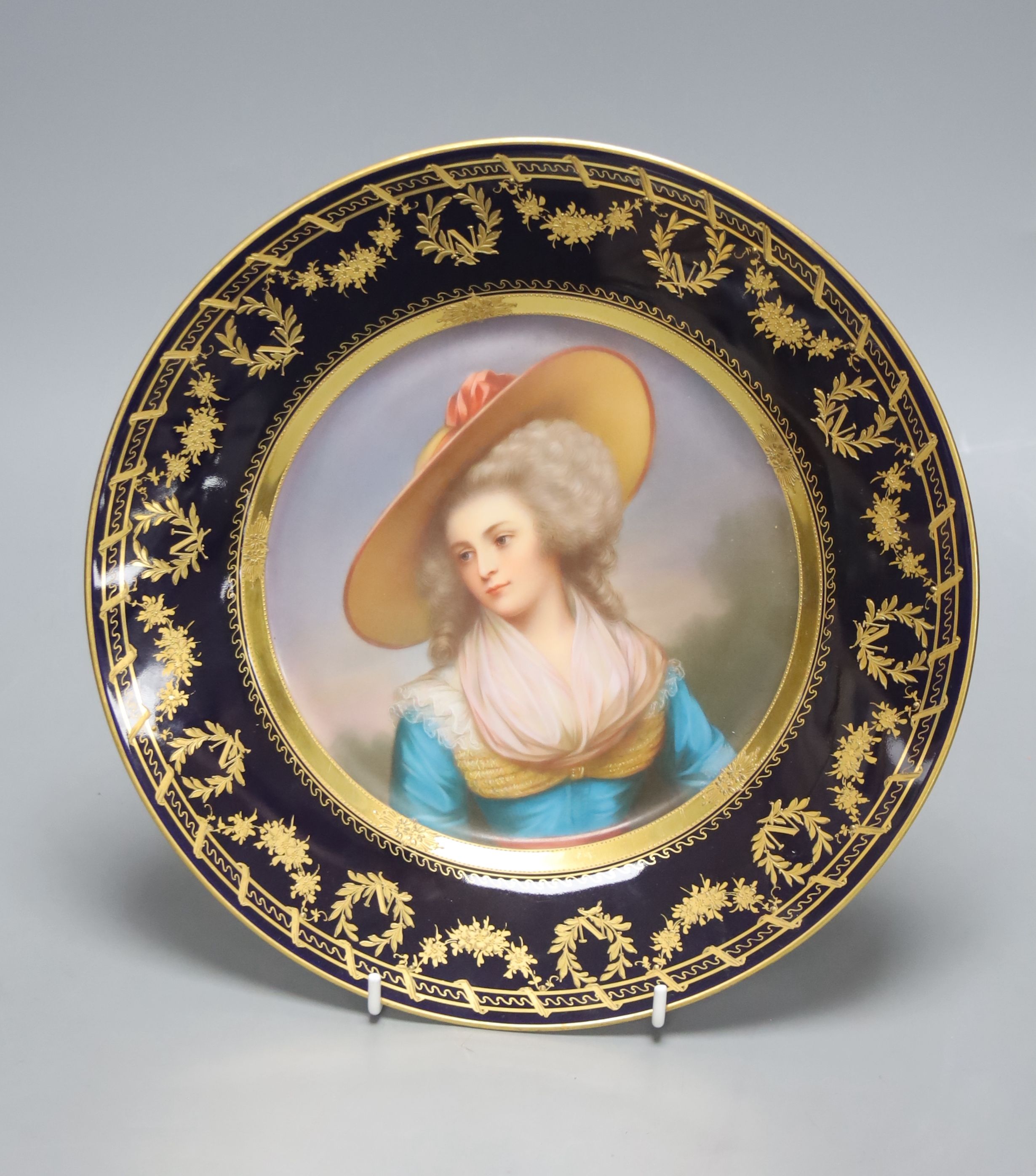 A Vienna style porcelain plate, c.1900, painted with a portrait of a lady wearing a hat, signed Weigel, diameter 25.5cm